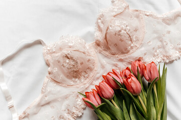 Pink bra, pink tulips on the bed. Women tender lingerie, underwear. Top view, close up. Flat lay, beauty blog or social media minimal concept. Present for Valentines, Women’s day