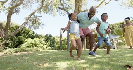 Happy african american grandparents with grandchildren playing football in garden, in slow motion - Powered by Adobe