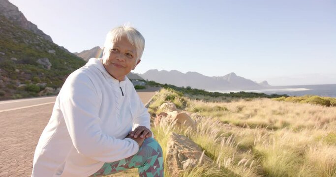 Happy senior biracial woman stretching in mountains on sunny day, in slow motion