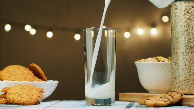 Fresh milk is poured into a glass from a jug against the background of bright light bulbs, slow motion. dairy products concept. Drinking fresh lactose-free milk in the morning. 