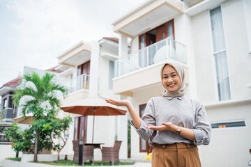 attractive Asian woman in hijab with hand gesture presenting in residential background