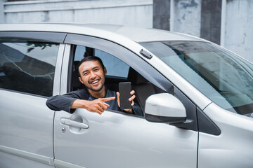 male driver holding a cell phone and pointing at the cell phone screen in the car