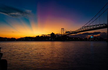 paisagem com raios coloridos no céu ocasionados pelo pôr do sol ponte Hercílio luz de...