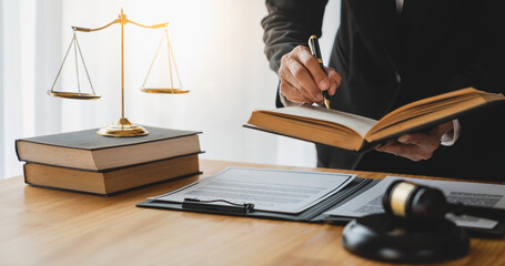 Asian female lawyer or legal advisor working on the scale of justice sitting at her desk and holding a pen to look at the information Detailed content about the scale of jurisprudence to study.