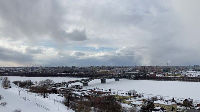 View from Fedorovsky Embankment in Nizhny Novgorod at the Kanavinsky Bridge over the frozen Oka river, the Upper and the Lower City with multi-storey houses covered by snow under a cloudy winter sky