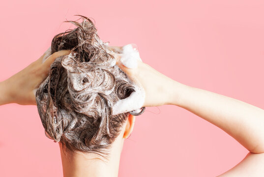 A girl washes her hair with shampoo on pink background, rear view