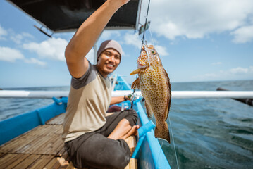 A grouper is hooked while fishing with a fishing rod in a small fishing boat