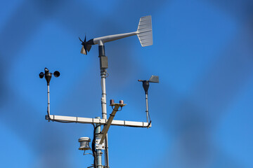 A wind monitor device with wind sentry anemometer to measure wind speed and direction, chain link fence shadow on the background. - Powered by Adobe