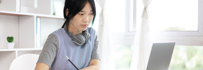 Asian woman taking notes in notebook while studying online in laptop at home, Video chat, Online communication , Stay home, New normal, Distance learning., Social distancing, Learn online..