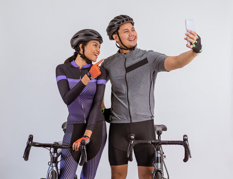 asian couple in cycling outfit taking selfie photo while standing beside their bicycles on isolated background