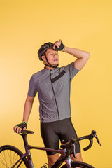 tired asian man swiping his sweat with his hand while standing beside his bicycle on isolated...