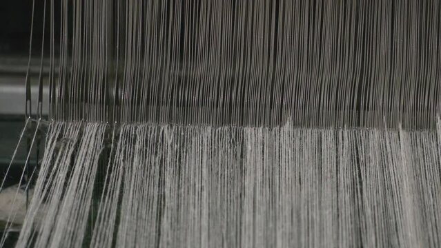 weaving loom, fabric weaving, weaving area thread needles long line. A close up of weaving machine. A loom machine for clothing or woven label. Weaving machine for garment industry.