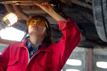 Asian woman auto mechanic work in vehicle repair shop, check and repair under body and suspension...