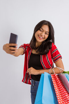 a beautiful asian girl taking selfie photo with her phone while bring the shopping bags on isolated background