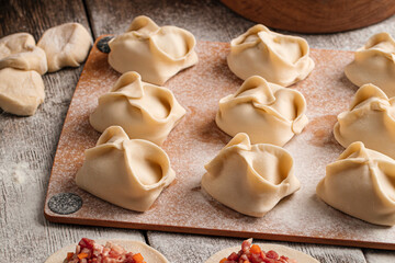 Semi-finished manti oriental dumplings on wooden board with flour