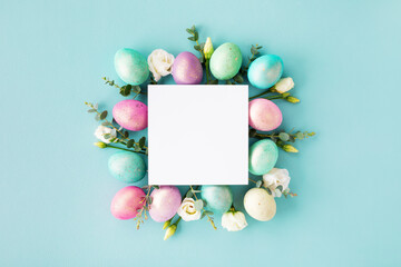 Naklejka na ściany i meble Easter spring concept. Top view photo of empty square blank, colorful eggs and flowers on pastel blue table.