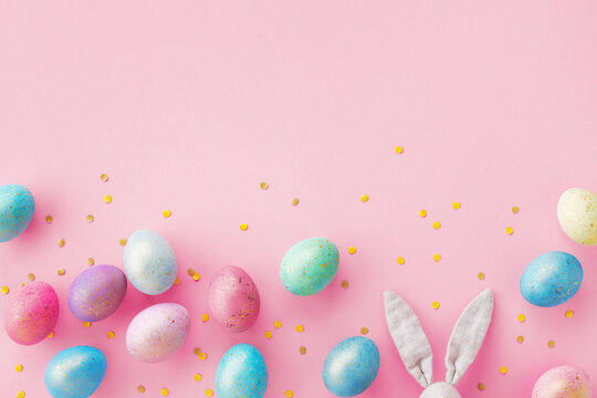 Holiday Easter background of colorful pastel Easter eggs and bunny ears on pink table top view.