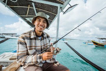 Asian angler smiles while holding a fishing rod on a small fishing boat