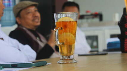 close up photo, cellphone and a glass of tea mixed with lemon placed on the office table, in a meeting atmosphere. which is useful for boosting immunity. Blurred background.