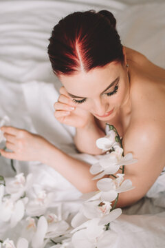 Photo shoot for women's day. The girl lies on the sheet. Naked female body in a sheet. Girl and orchids. Girl with flowers.