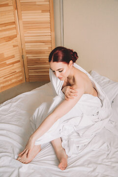 Photo shoot for women's day. The girl lies on the sheet. Naked female body in a sheet. Girl and orchids. Girl with flowers.