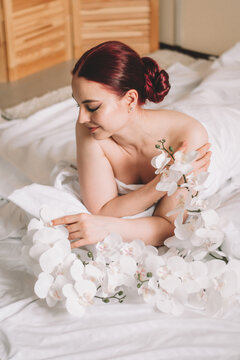 Photo shoot for women's day. The girl lies on the sheet. Naked female body in a sheet. Girl and orchids. Girl with flowers.