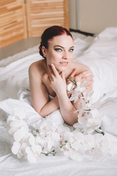 Photo shoot for women's day. The girl lies on the sheet. Naked female body in a sheet. Girl and orchids. Girl with flowers.