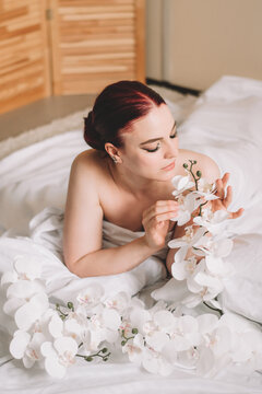 Photo shoot for women's day. The girl lies on the sheet. Naked female body in a sheet. Girl and orchids. Girl with flowers.