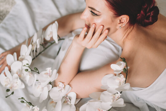 Photo shoot for women's day. The girl lies on the sheet. Naked female body in a sheet. Girl and orchids. Girl with flowers.
