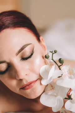 Photo shoot for women's day. The girl lies on the sheet. Naked female body in a sheet. Girl and orchids. Girl with flowers.