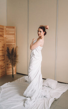 Photo shoot for women's day. The girl lies on the sheet. Naked female body in a sheet. Girl and orchids. Girl with flowers.