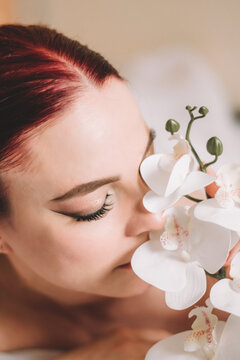 Photo shoot for women's day. The girl lies on the sheet. Naked female body in a sheet. Girl and orchids. Girl with flowers.