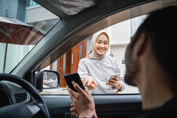 Asian veiled woman points at transportation driver's cell phone when he comes to pick her up