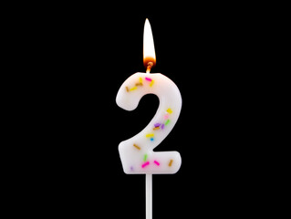 White decorated burning birthday candle isolated on black background, number 2