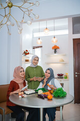 happy young asian woman with hijab cooking in the kitchen while looking at internet on mobile phone for menu today