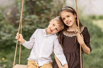 a little boy and a girl are resting, a brother and sister are swinging on a swing in the spring in the garden of a country house. concept of village life