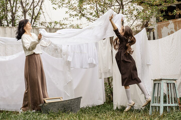 a girl of primary school age helps her mother hang freshly laundered laundry on ropes in the spring...