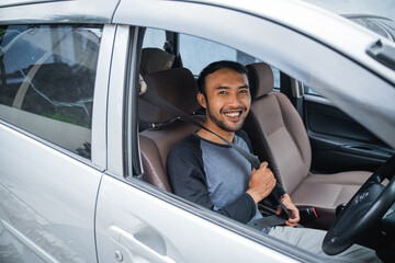 Asian male driver smiles after fastening his seat belt before driving off in a car