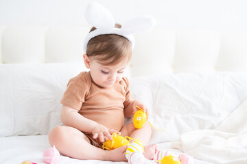 cute funny baby with bunny ears and colorful Easter eggs on bed at home