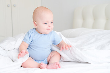 portrait of smiling baby boy with big blue eyes in bodysuit on white bedding. Healthy newborn child