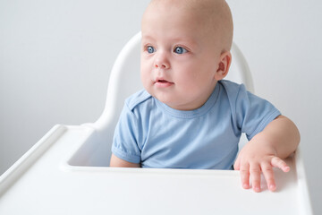 bald smiling baby boy 3 months sitting in baby chair on white background