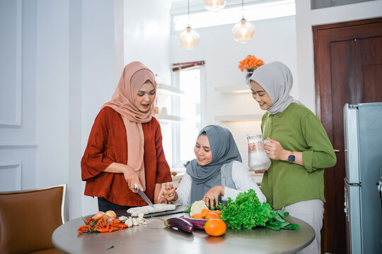 woman wearing hijab with best friend preparing food for dinner in the kitchen