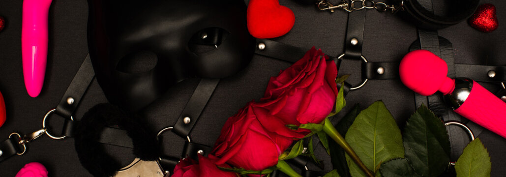 Various sex toys set on a black background. An ad for a sex shop. Top view. Spring. Roses.Horizontal wide photo subtitle, cover. copy-space
