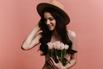 Photo portrait of a young woman smiling, holding a bouquet of tulips, isolated against a pastel pink background.