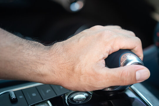 Action of a car driver hand is controlling and shifting the gear's shifter. Car driving activity scene photo. Close-up and selective focus.
