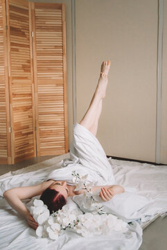 Photo shoot for women's day. The girl lies on the sheet. Naked female body in a sheet. Girl and orchids. Girl with flowers.