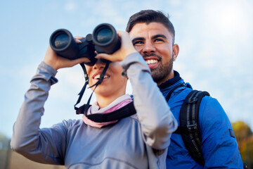 Nature, binoculars and couple hiking together for fitness, exercise and fresh air on an adventure trail. Travel, fun and young man and woman trekking and sightseeing on a mountain while on vacation.