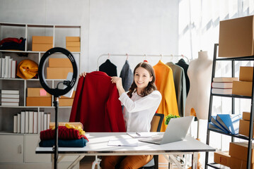 Beautiful Asian lady blogger showing clothes in front of the camera to recording vlog video live...