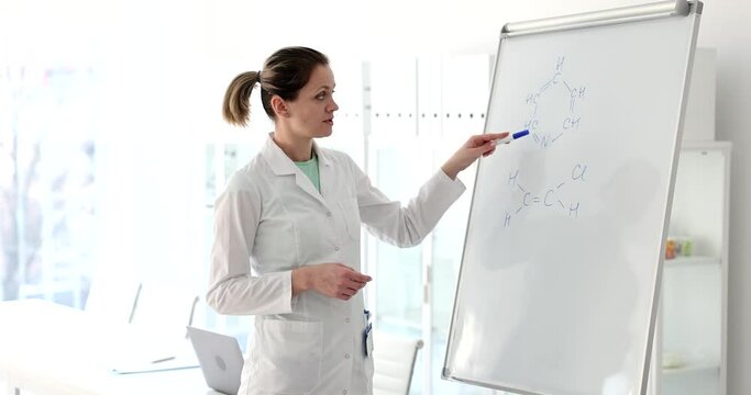 Female scientist teacher writes and explains formula on white board in laboratory