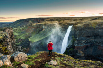 Haifoss waterfall flowing in volcanic canyon and traveler taking a picture among the Icelandic Highlands in summer